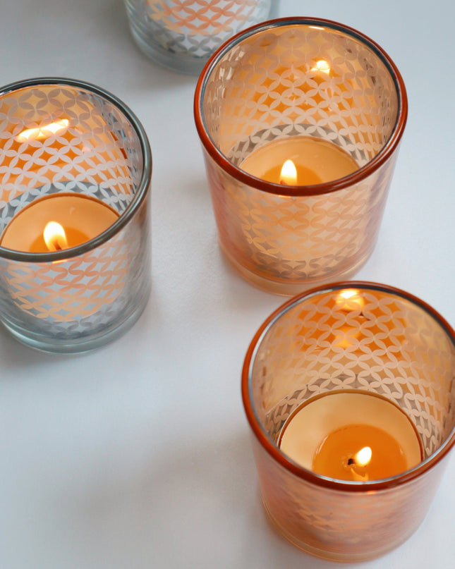 Four glass gold and silver candle holders with lit candles on a light background