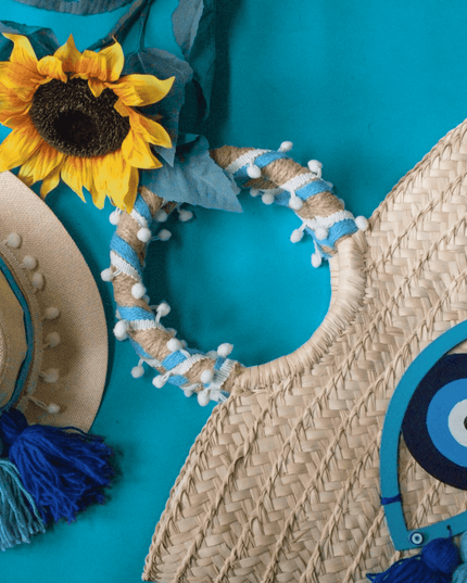 Woven hat with blue tassels and decorative headband and evil eye beach bag with wooden accents on a teal background
