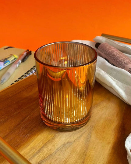 gold glass candle holder on a wooden surface with an orange background