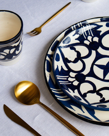 Black and white patterned ceramic plates and cups with gold cutlery on a light gray surface.