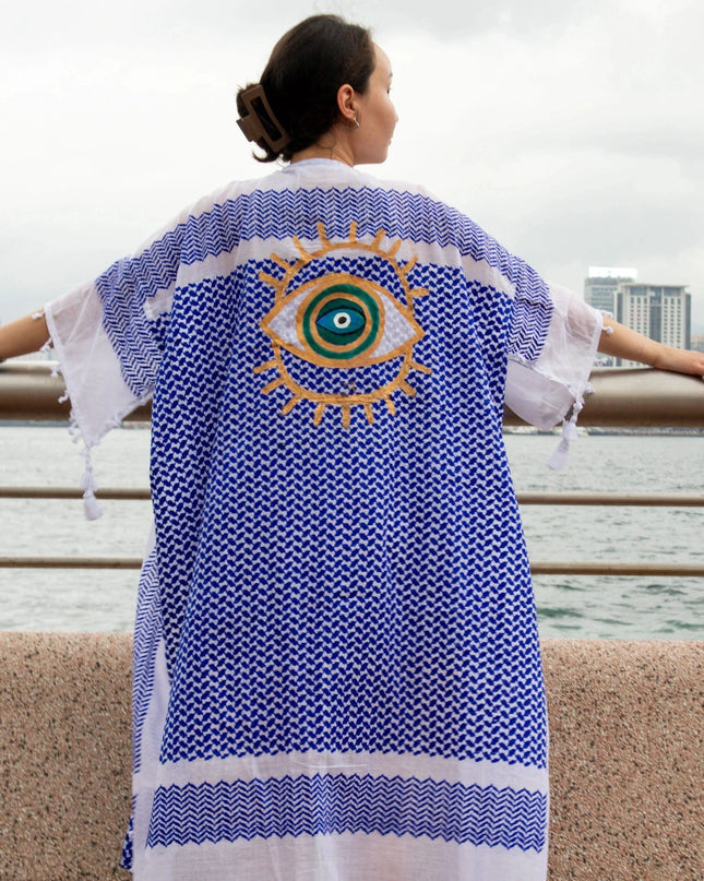 Woman Wearing A Blue And White Patterned Kaftan With A Hand-Painted Evil Eye Design