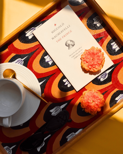 Book titled 'Niccolo Machiavelli The Prince' on a decorative hand-painted floral tray with cookies and a cup.