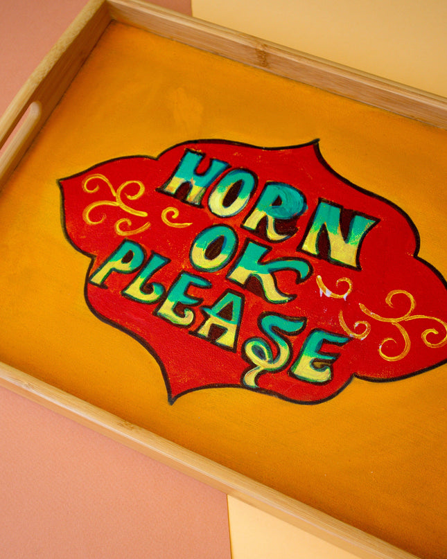 Wooden tray with a colorful sign reading 'Horn Ok Please' on a pink and beige background