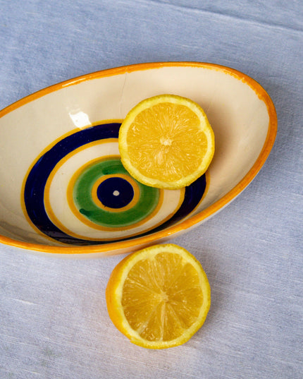 Sliced lemons on a decorative ceramic bowl with hand-painted evil eye design on a gray surface