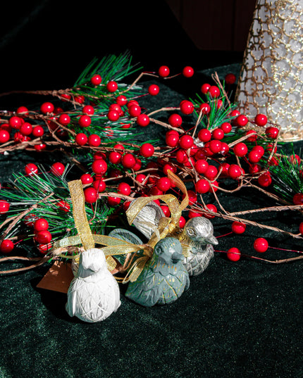 Decorative Christmas bird ornaments with red berries, greenery, and small ornaments on a dark surface