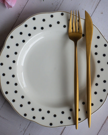 Polka dot plate with gold fork and knife on a white wooden surface with pink flowers.