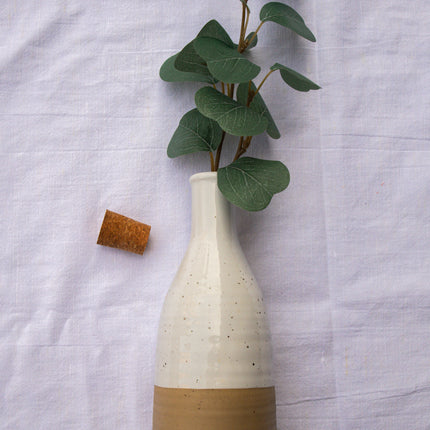 Casa Duniya's Yahi Ceramic Bottle in White and Beige with Leaves on a White Linen Background
