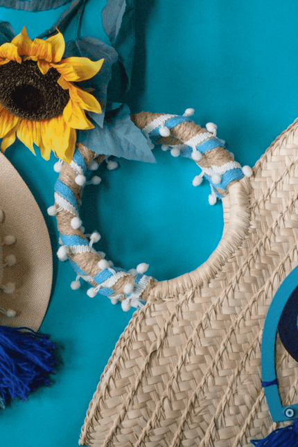 Casa Duniya's Hand Embroidered Evil Eye Beach Bag and Hat on a Turquoise Background with a sunflower as decor