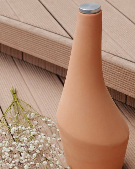 Terracotta-colored vase with a metallic cap on a wooden deck
