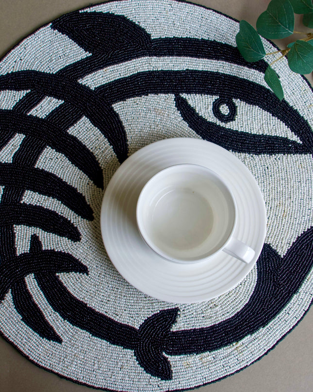 Round placemat with black abstract design on a gray surface with a white cup and saucer.
