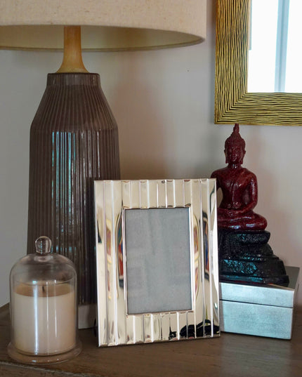 Decorative items on a wooden surface including a lamp, striped silver photo frame, and small statue.