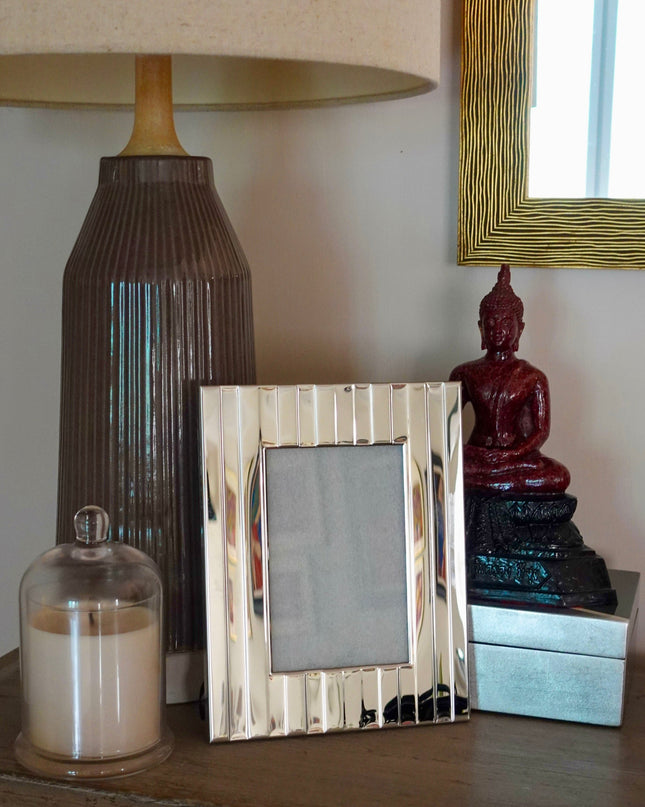 Decorative items on a wooden surface including a lamp, striped silver photo frame, and small statue.
