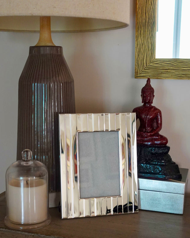 Decorative items on a wooden surface including a lamp, striped silver photo frame, and small statue.