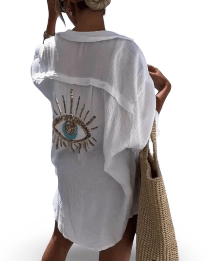 White sheer shirt with eye design worn by a person, holding a woven beach bag.