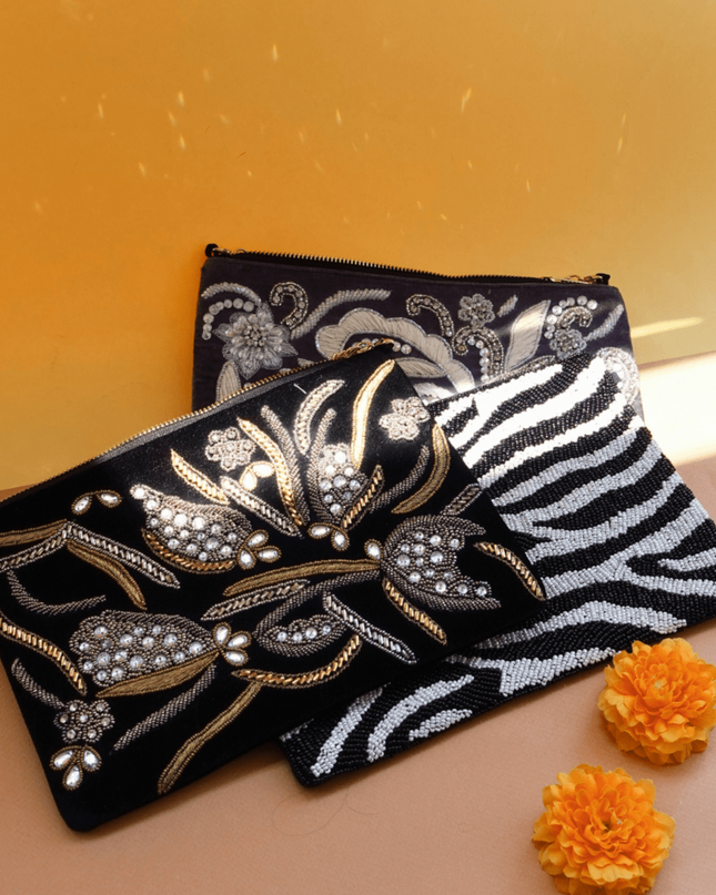 two beaded clutches with floral patterns and one zebra pattern on a beige surface with orange flowers.