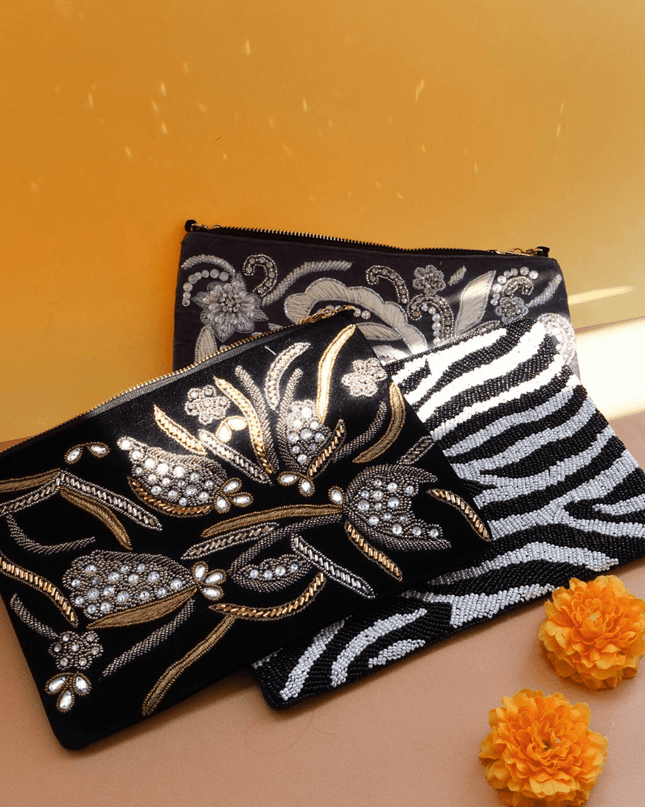 two beaded clutches with floral patterns and one zebra pattern on a beige surface with orange flowers.