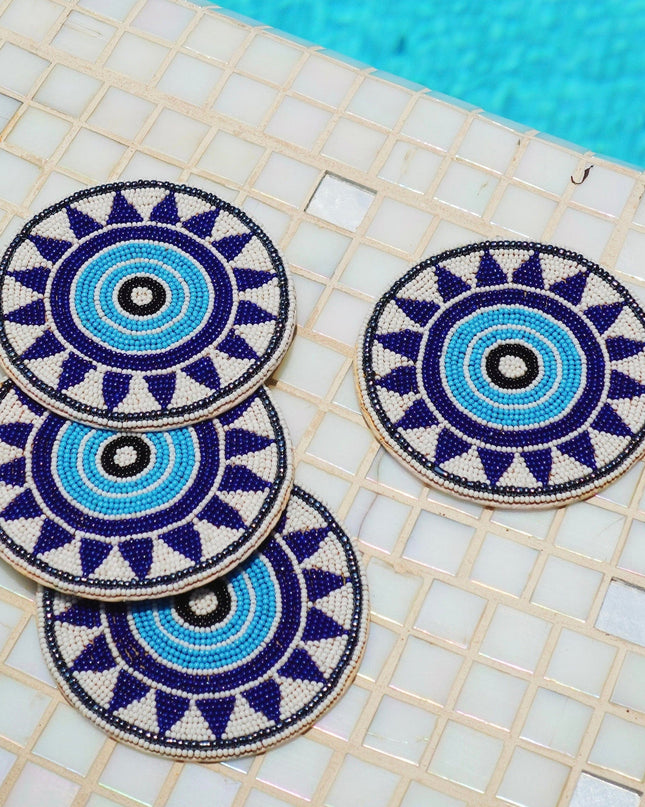 Four decorative beaded coasters with blue and white evil-eye patterns on a tiled poolside surface.