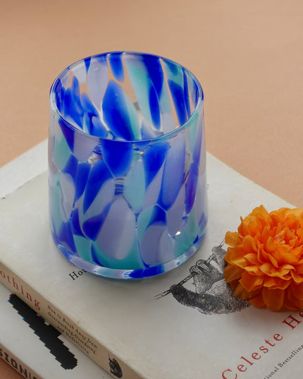 Blue blown glass water tumbler on a book with an orange flower