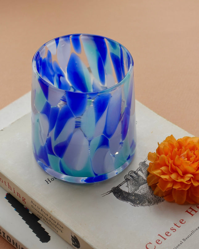 Blue blown glass water tumbler on a book with an orange flower