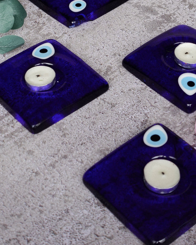 Four blue glass evil eye candle holders with candles on a textured surface.