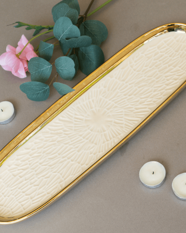 Decorative tray with textured surface and gold rim on a neutral background with candles and flowers.
