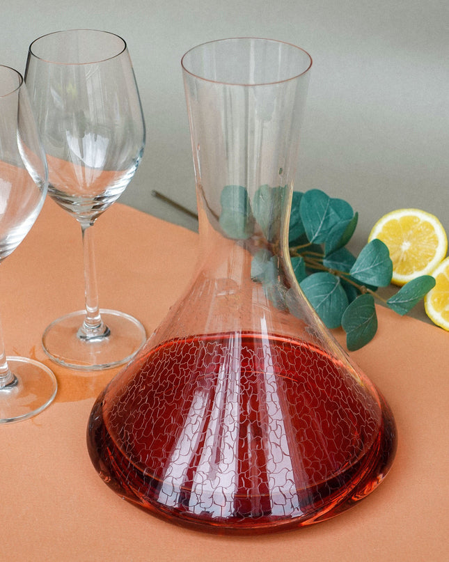 Glass decanter with cracked design on a peach surface with wine glasses and lemons.