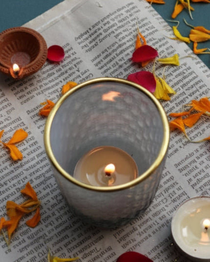 Gray Patterned Candle Holder on a newspaper with flower petals and candles on a dark green background