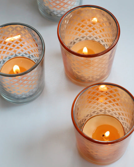Four glass gold and silver candle holders with lit candles on a light background