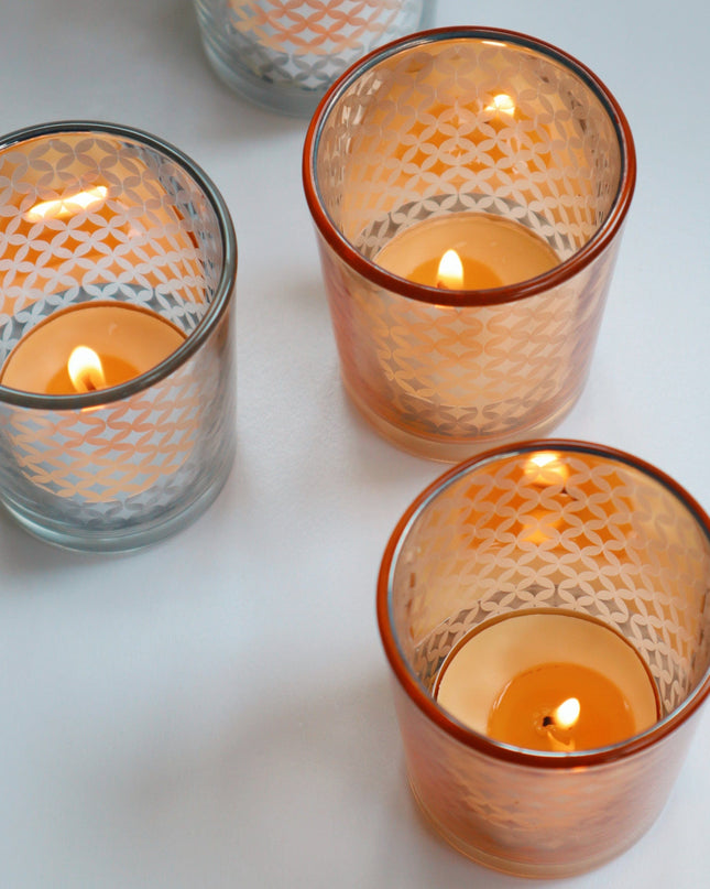 Four glass gold and silver candle holders with lit candles on a light background