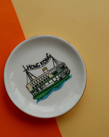 Small white dish with a drawing of a ferry and 'Hong Kong' text on an orange and beige background