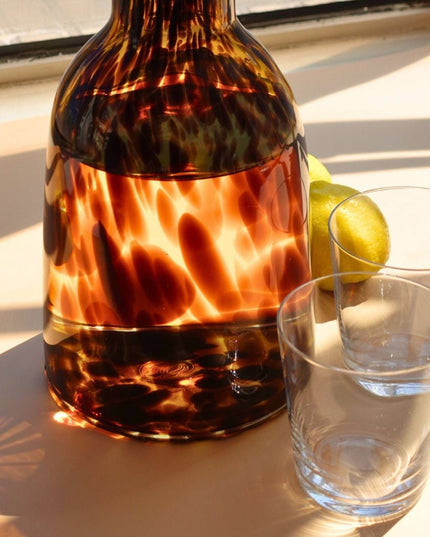 leopard-patterned decanteron a windowsill with a glass of water and a lemon.