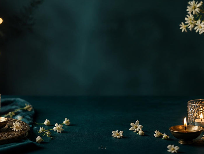 Diwali table setting on deep teal fabric with brass diyas, glass candle holders and white flowers