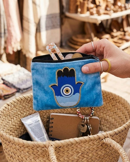 Sofia Cosmetic Pouch with hamsa design held over a woven basket