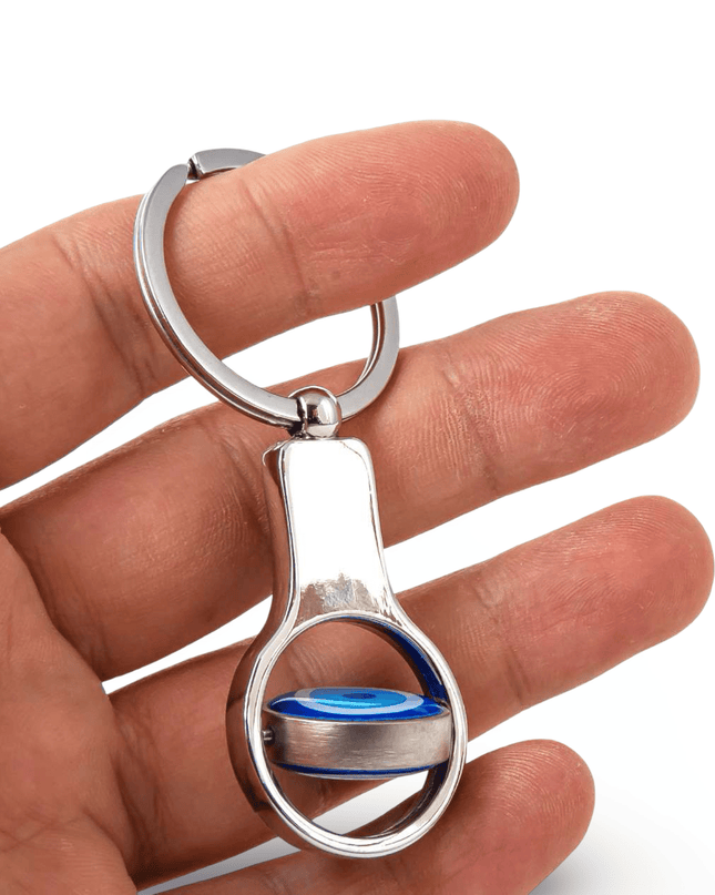 Silver keychain with a blue evil eye movable accent held in a hand against a white background