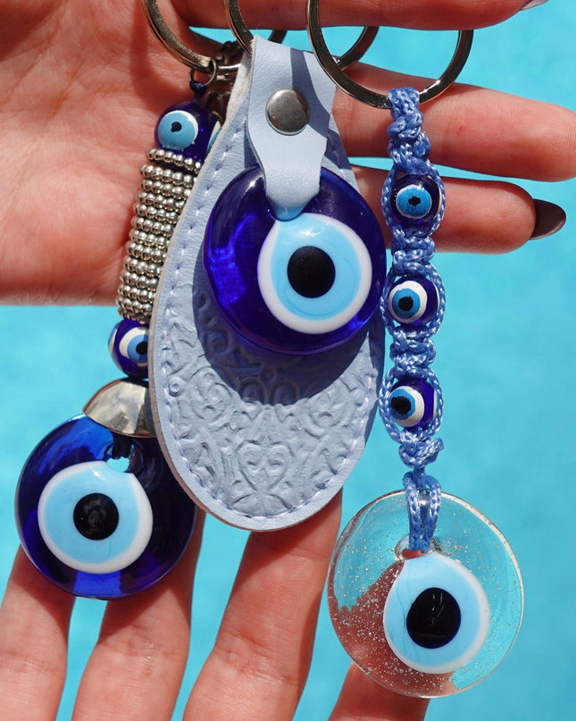 Hand holding three keychains with eye designs against a blue background
