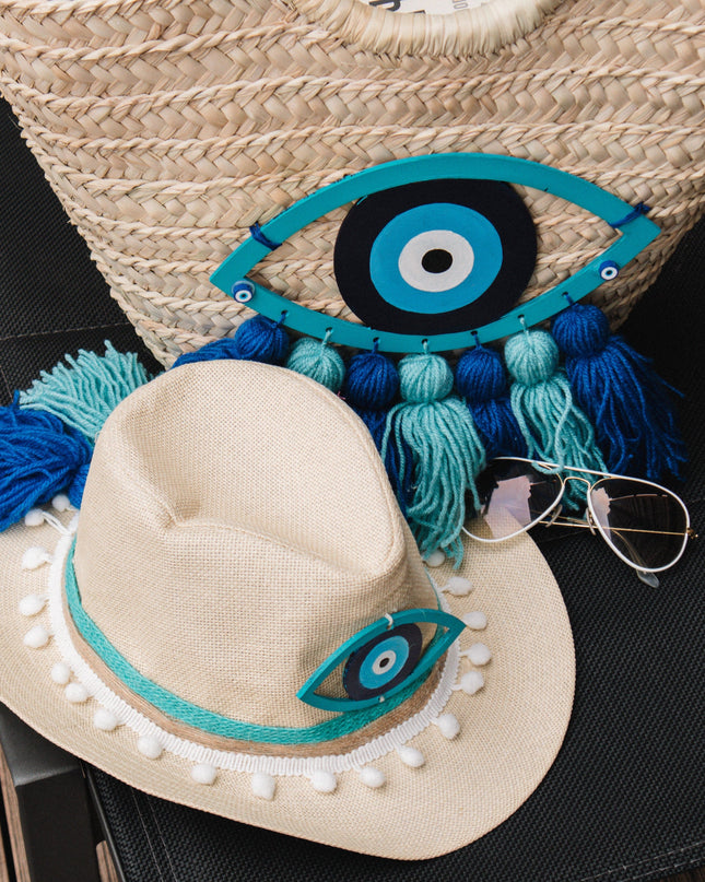 Straw bag and hat with decorative evil eye design on a dark surface
