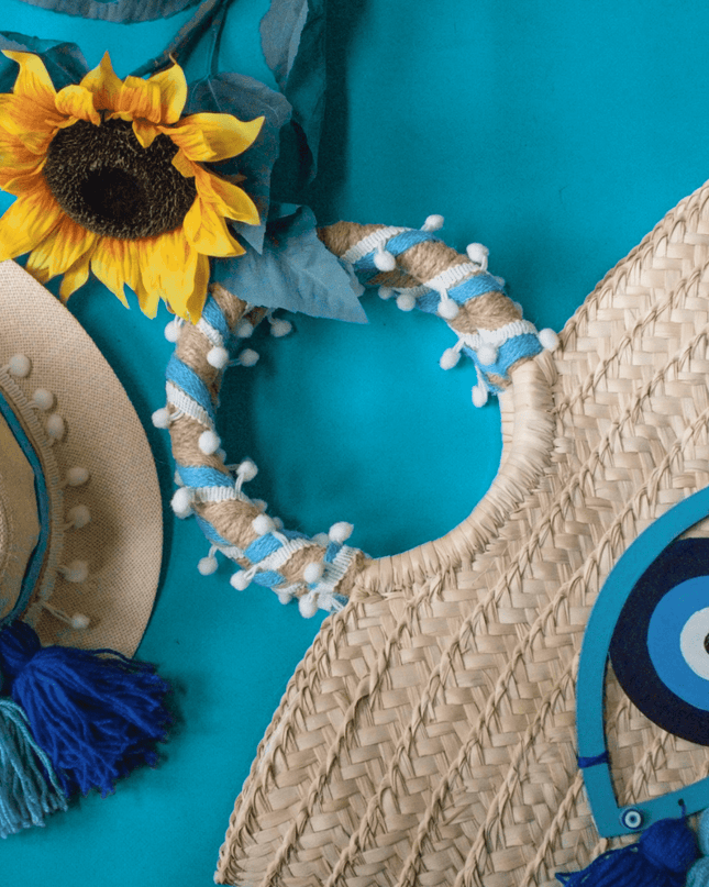 Woven hat with blue tassels and decorative headband and evil eye beach bag with wooden accents on a teal background