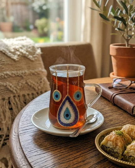Close-up of a hand-painted blue and gold evil eye on a clear glass tea cup with handle