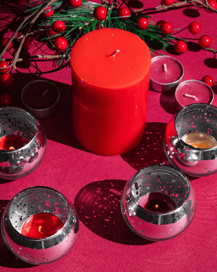 Red candle and silver candle holders on a red surface with greenery and berries.