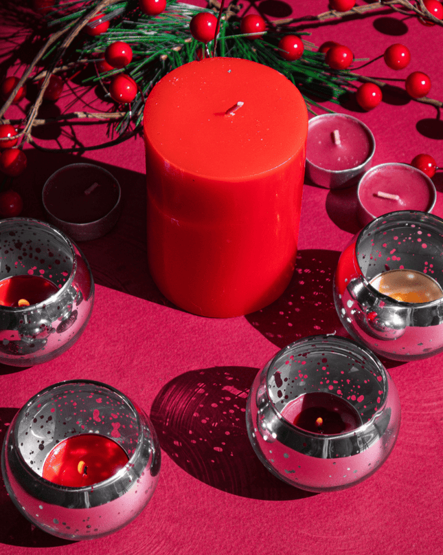 Red candle and silver candle holders on a red surface with greenery and berries.