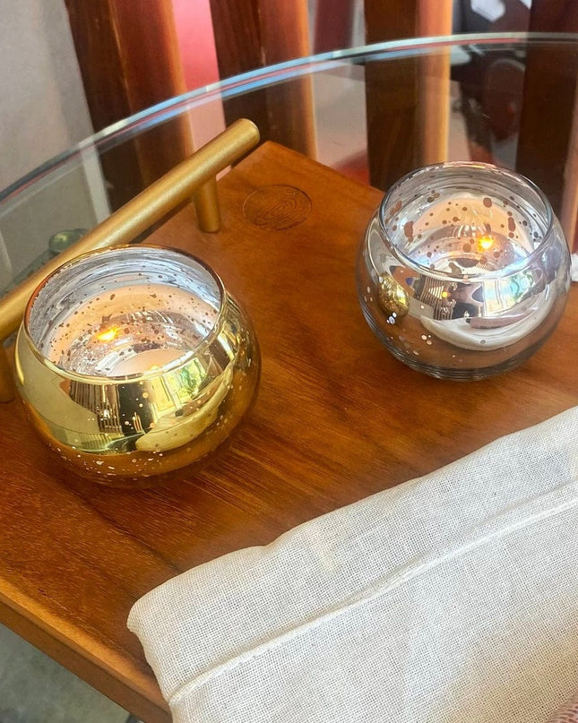 Two small glass candle holders with candles on a wooden table.