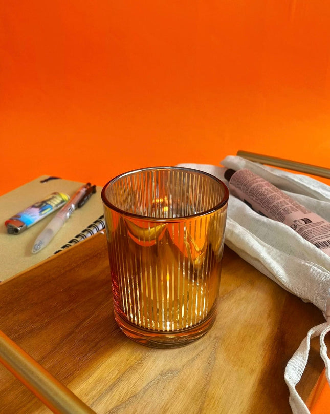 gold glass candle holder on a wooden surface with an orange background