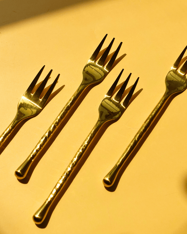 Four gold forks arranged on a yellow background