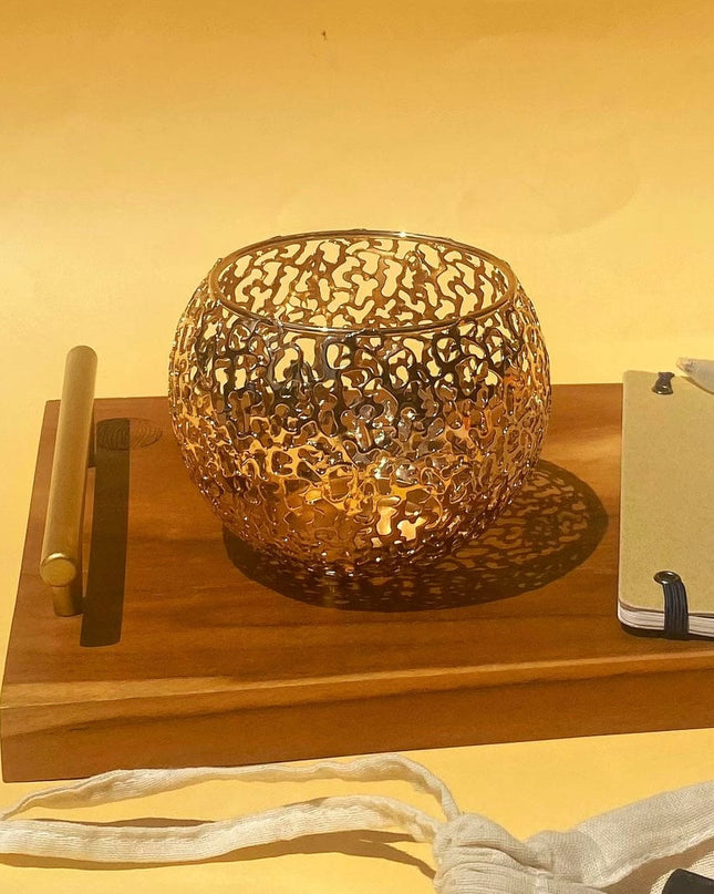 Decorative metal candle holder on a wooden tray with a warm glow against a yellow wall.