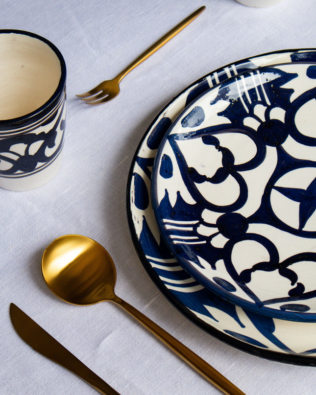 Black and white patterned ceramic plates and cups with gold cutlery on a light gray surface.