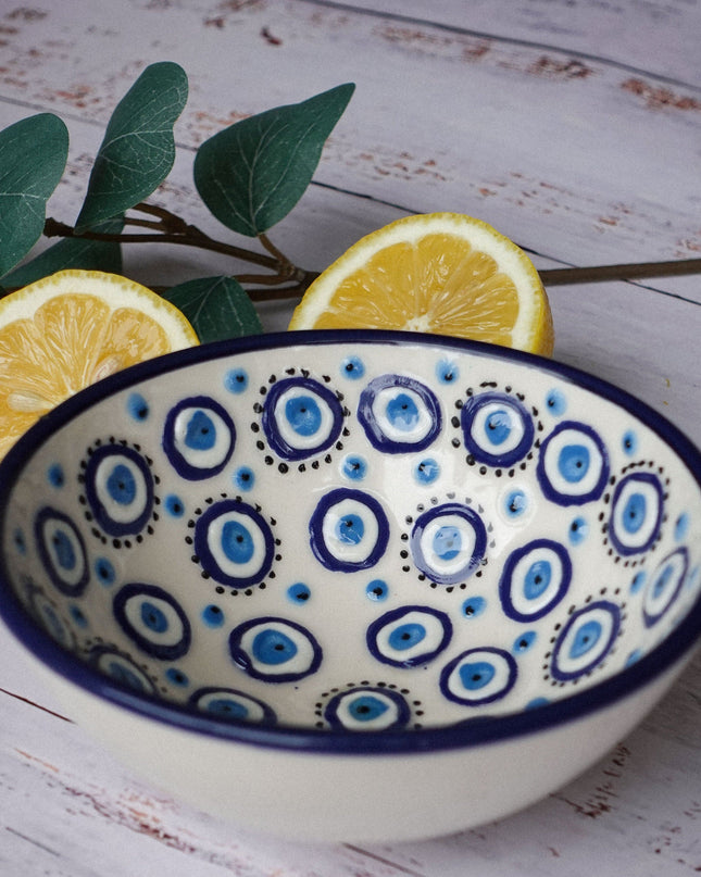 Ceramic bowl with blue and white evil eye pattern on a wooden surface with lemons and leaves.