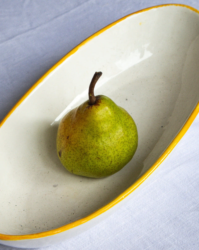 Green pear on a white ceramic dish with yellow rim on a light gray background