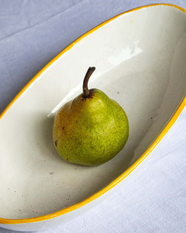 Green pear on a white ceramic dish with yellow rim on a light gray background