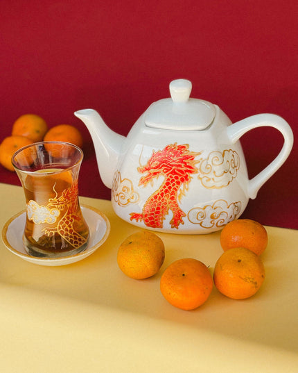 Teapot with dragon design, glass of tea, and oranges on a yellow surface with red background