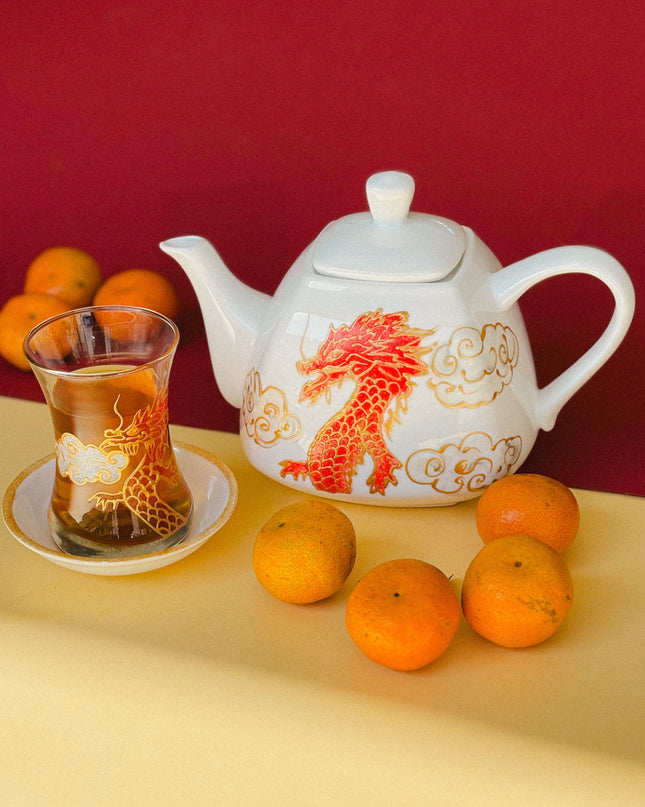 Teapot with dragon design, glass of tea, and oranges on a yellow surface with red background